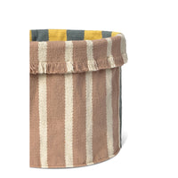 A woven fabric storage basket with vertical stripes in brown, cream, and mustard yellow, featuring a fringed top edge and a dark gray side panel, shown on a white background.