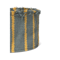 A close-up of a woven basket in a muted blue-gray color with vertical mustard yellow stripes and frayed fringe along the top edge, shown on a plain white background.