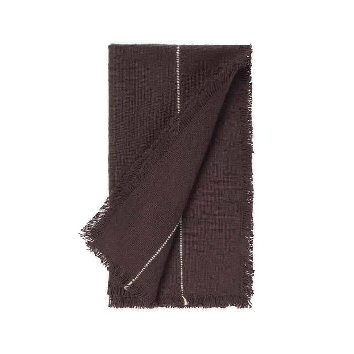 A dark brown woven napkin with fringed edges and a thin white stitched detail, folded neatly on a solid white background.