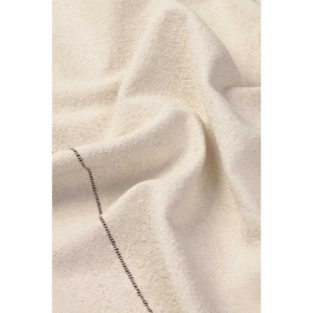 A close-up of draped off-white or cream napkin with a visible dark stitched seam running diagonally through the lower-left area.
