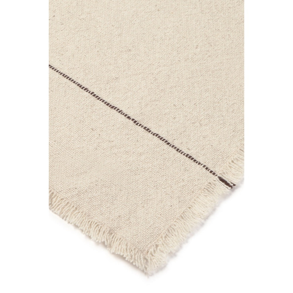 Close-up of a cream-colored woven napkin, showing a textured weave and a fringed edge with a dark stitched detail.