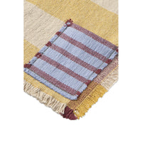 A close-up of a woven textile with a large patch pocket. The fabric features a mustard yellow and cream striped pattern, with a central pocket in light blue and dusty rose stripes, finished with cream fringe.