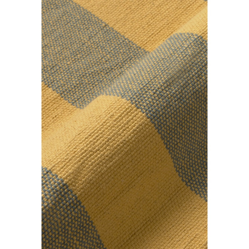 Close-up of a woven textile with a checkered pattern in mustard yellow and muted blue-gray, showing the fabric texture and fold details.