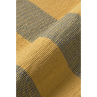 Close-up of a woven textile with a checkered pattern in mustard yellow and muted blue-gray, showing the fabric texture and fold details.