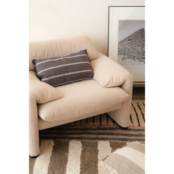 A beige upholstered armchair in a styled living room setting, featuring a brown and white striped throw pillow and a patterned rug.