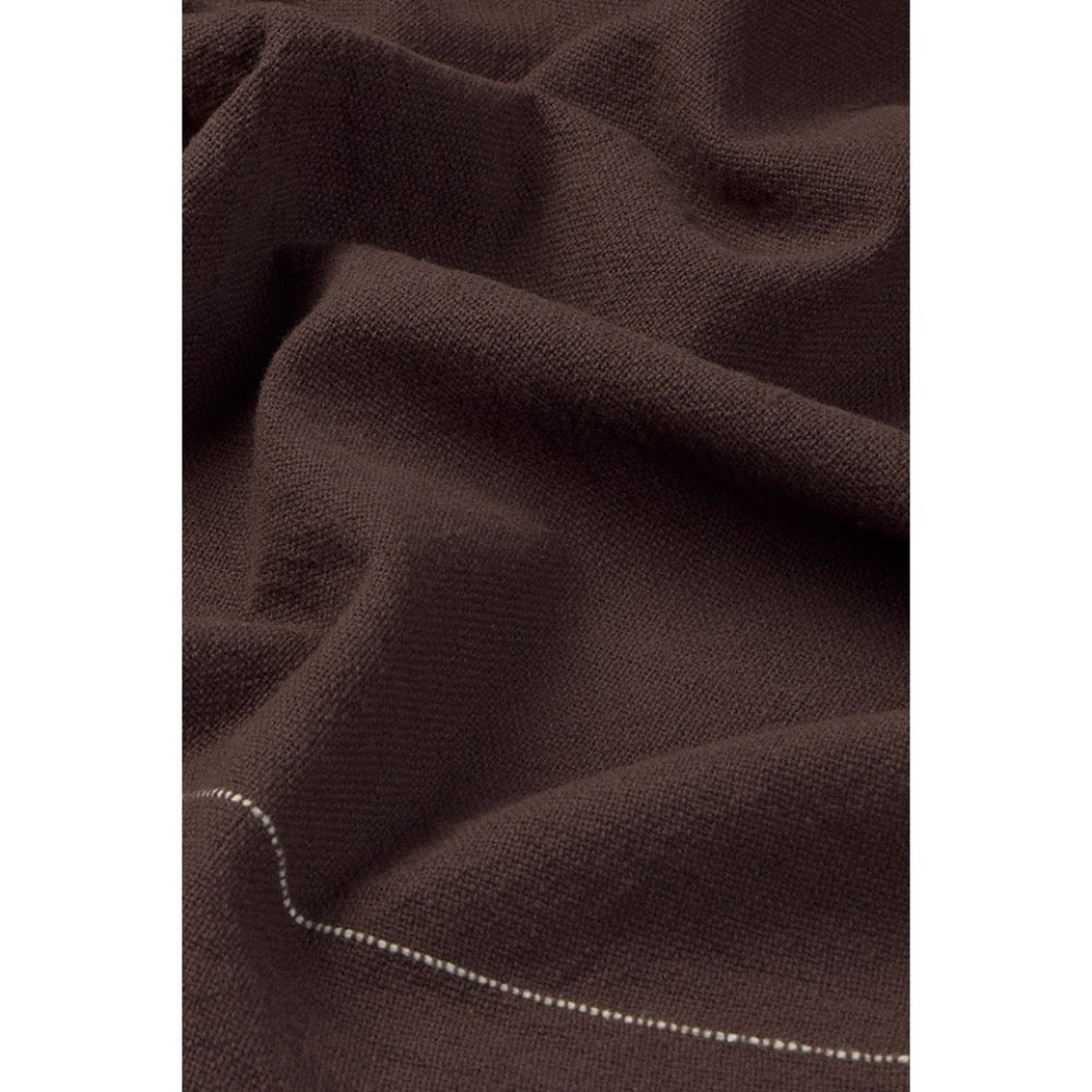 A close-up of dark brown tablecloth with a fine white dotted line running alongh the lower edge.