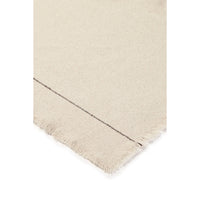 Close-up of a cream-colored woven tablecloth, showing a fringed edge and a thin dark stitched detail against a white background.