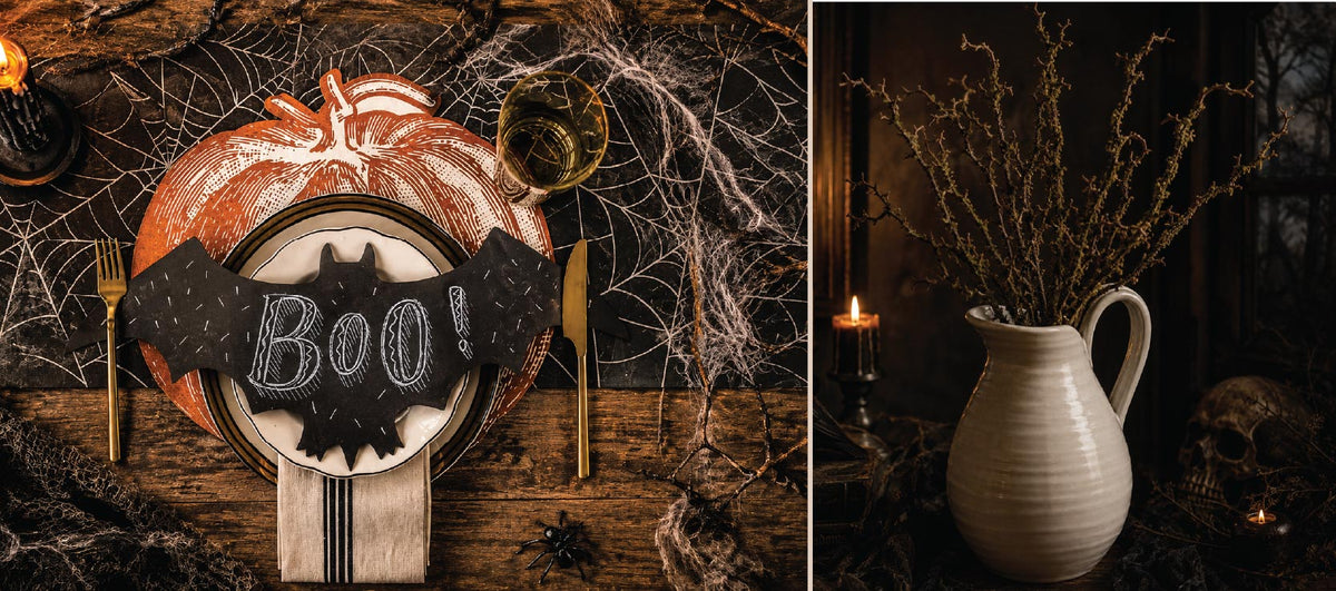 Halloween table with “Boo!” bat decor, pumpkin plate, cobwebs, candles, and a white pitcher with twigs.