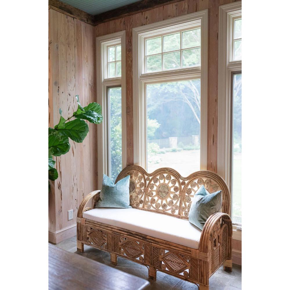 Wicker bench with cushions in a room with wooden walls and large windows.