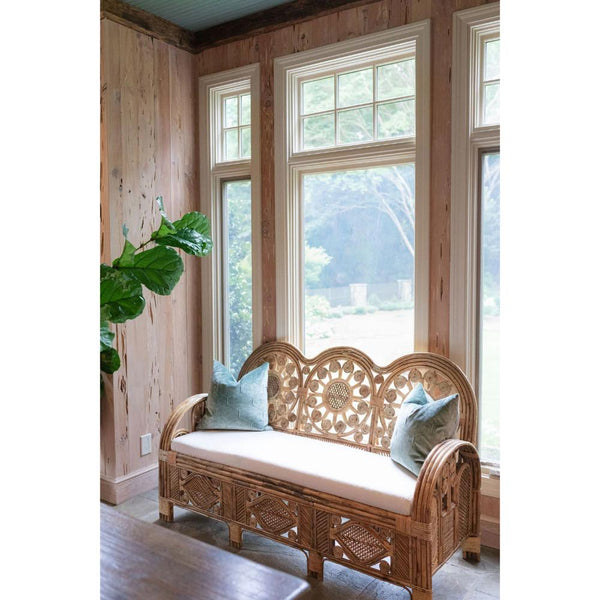 Wicker bench with cushions in a room with wooden walls and large windows.