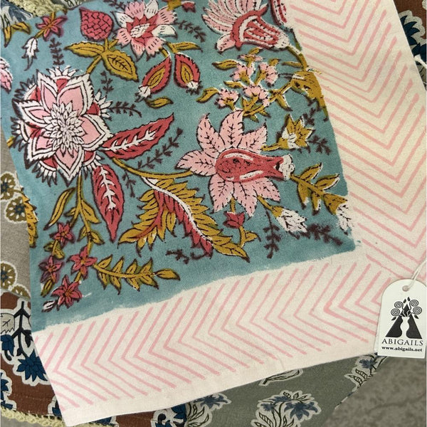 Blue fabric with pink and yellow floral embroidery beside Abigails' Seaside Bouquet Cabana Napkins (set of 8).