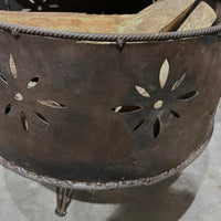 Metal fire pit with decorative cutouts and wooden logs on a concrete surface
