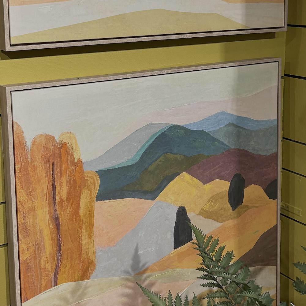 Two framed landscape paintings on a yellow wall.