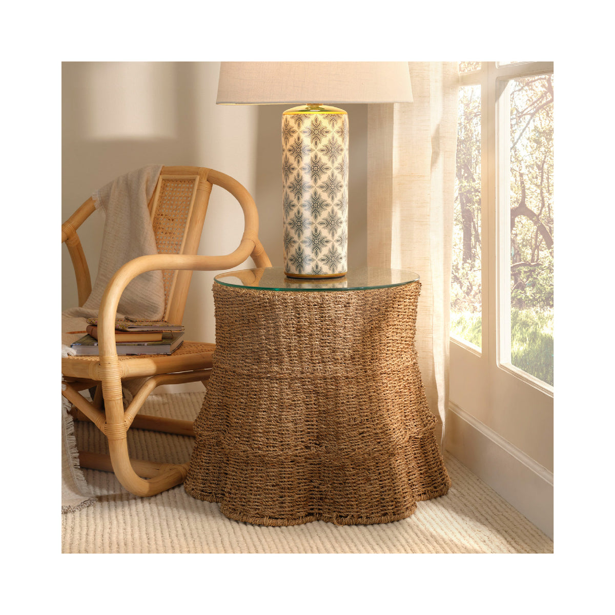 Wicker side table with glass top next to a chair in a room with a lamp and window.