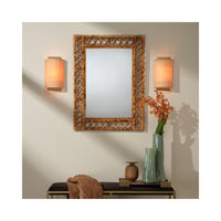 Decorative mirror with ornate frame on a wall with two wall sconces and a vase with flowers.