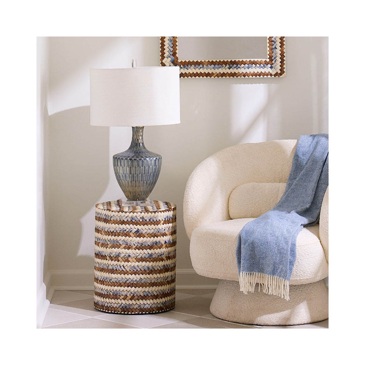 Decorative lamp on a textured side table next to a beige armchair with a blue blanket.