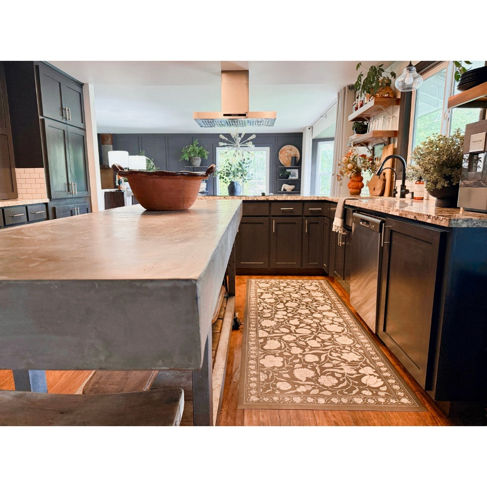 Modern kitchen with dark cabinets, concrete island, and Spicher and Company floral vinyl mat on wood floors.