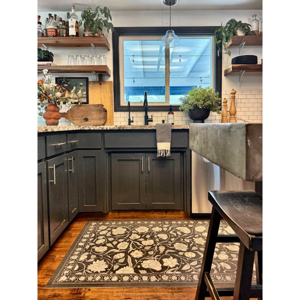 A modern kitchen with dark cabinets, open shelves, and a Spicher and Company floral vinyl mat under the sink window.
