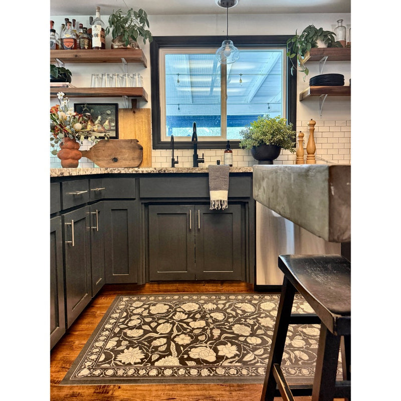 A modern kitchen with dark cabinets, open shelves, and a Spicher and Company floral vinyl mat under the sink window.