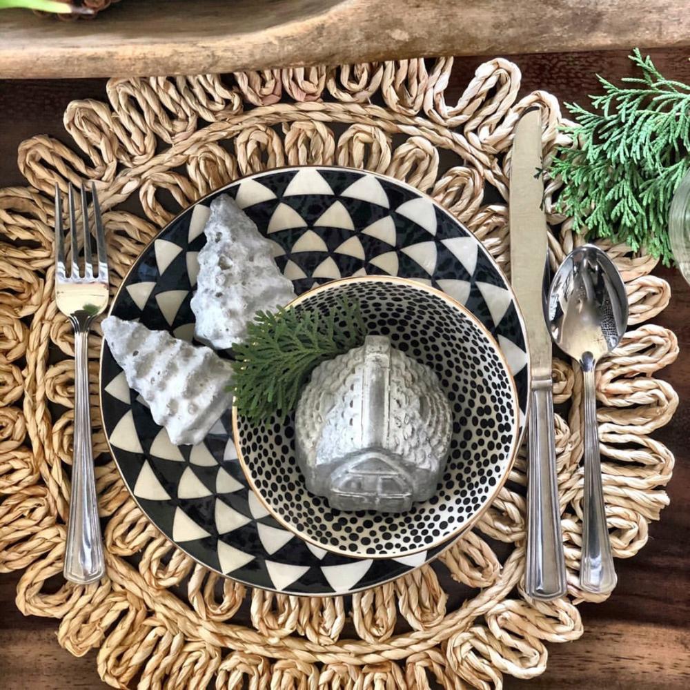 Decorative table setting with black and white patterned plates, silver cutlery, and decorative elements on a woven placemat.