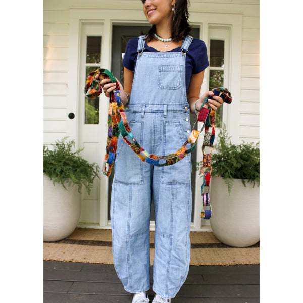 A girl holding a handmade patchwork fabric garland made of colorful stitched fabric strips in orange, green, blue, brown, and red.