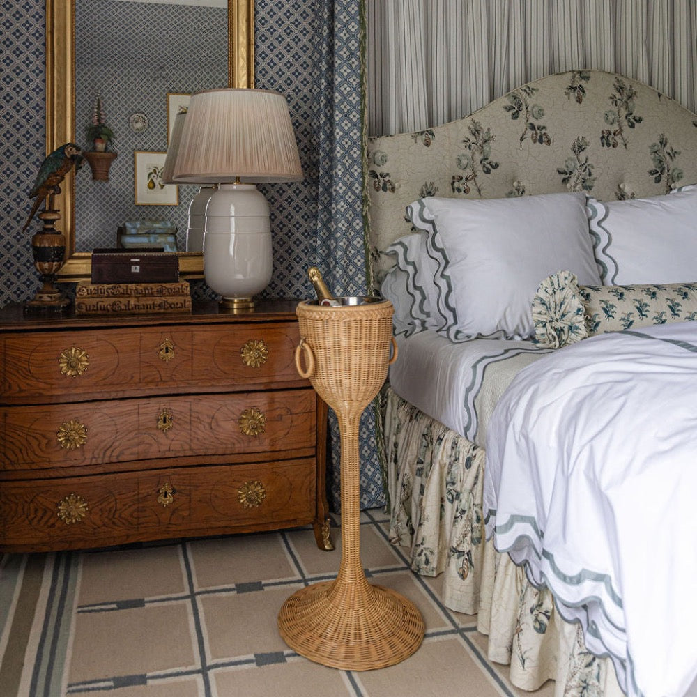 Bedroom with wooden dresser, lamp, and wicker champagne stand.