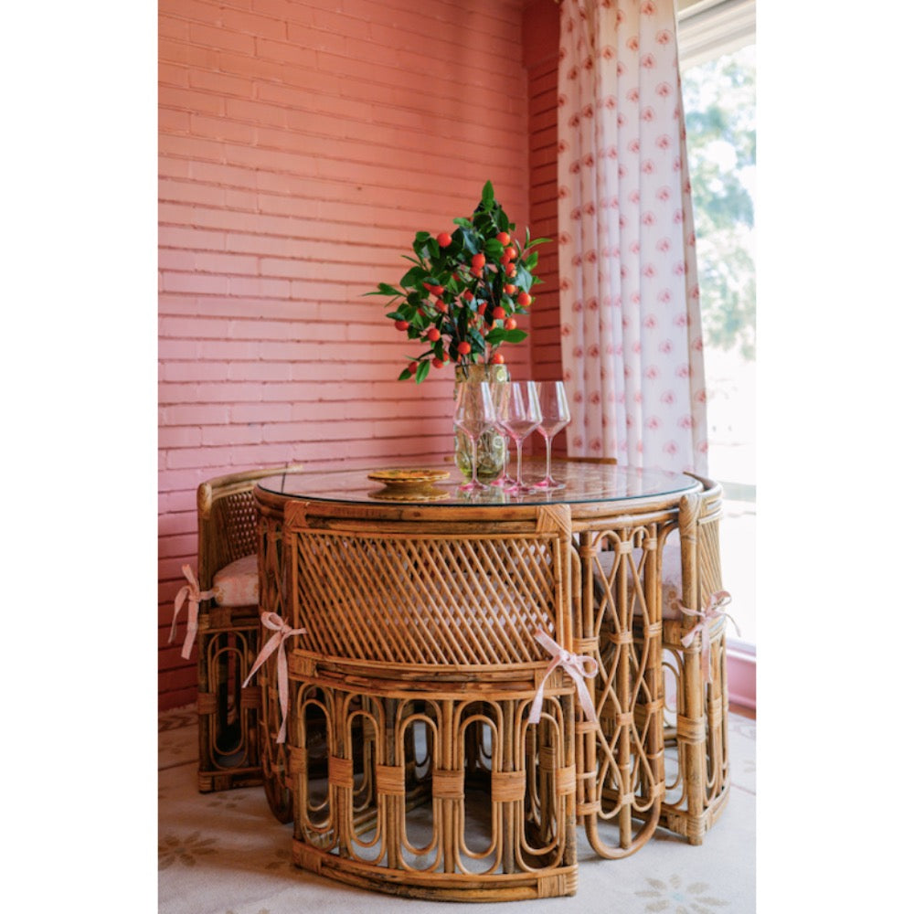 Wicker dining table with chairs against a pink wall