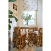 Rattan dining set with a glass table in a room with floral wallpaper.