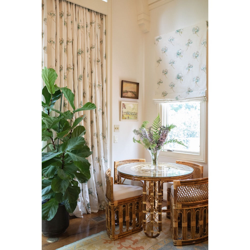 Rattan chairs and table in a room with floral curtains and a plant.