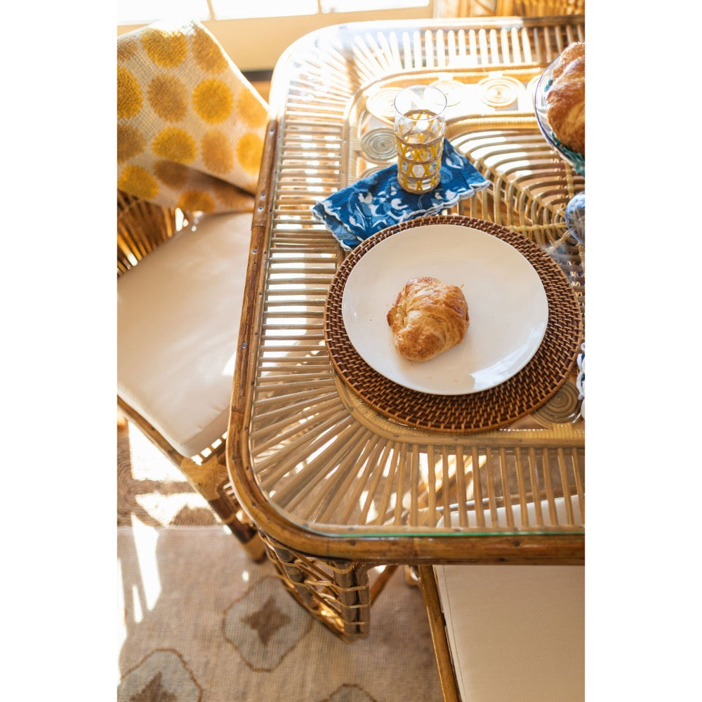 Rattan table with a plate of food and a glass on a light-colored floor.