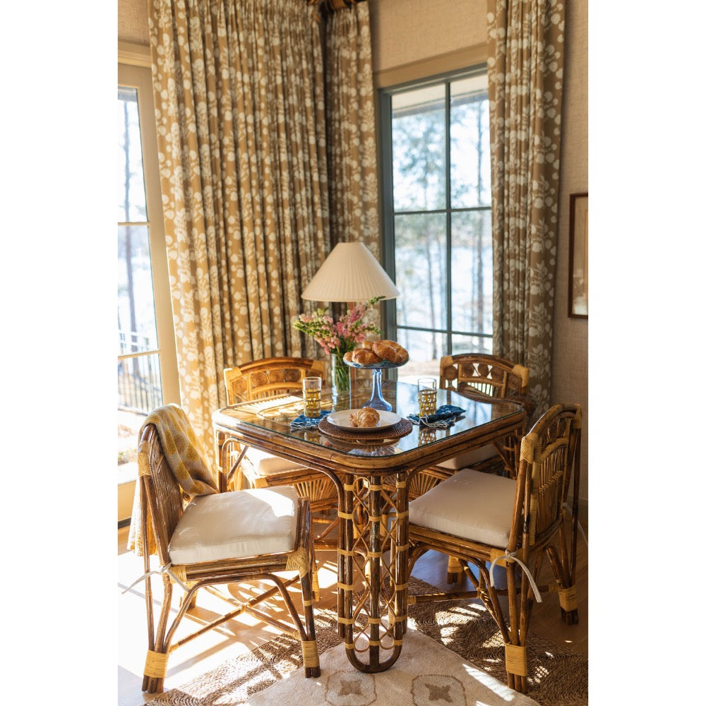 Dining room with a rattan table and chairs in front of large windows with curtains.