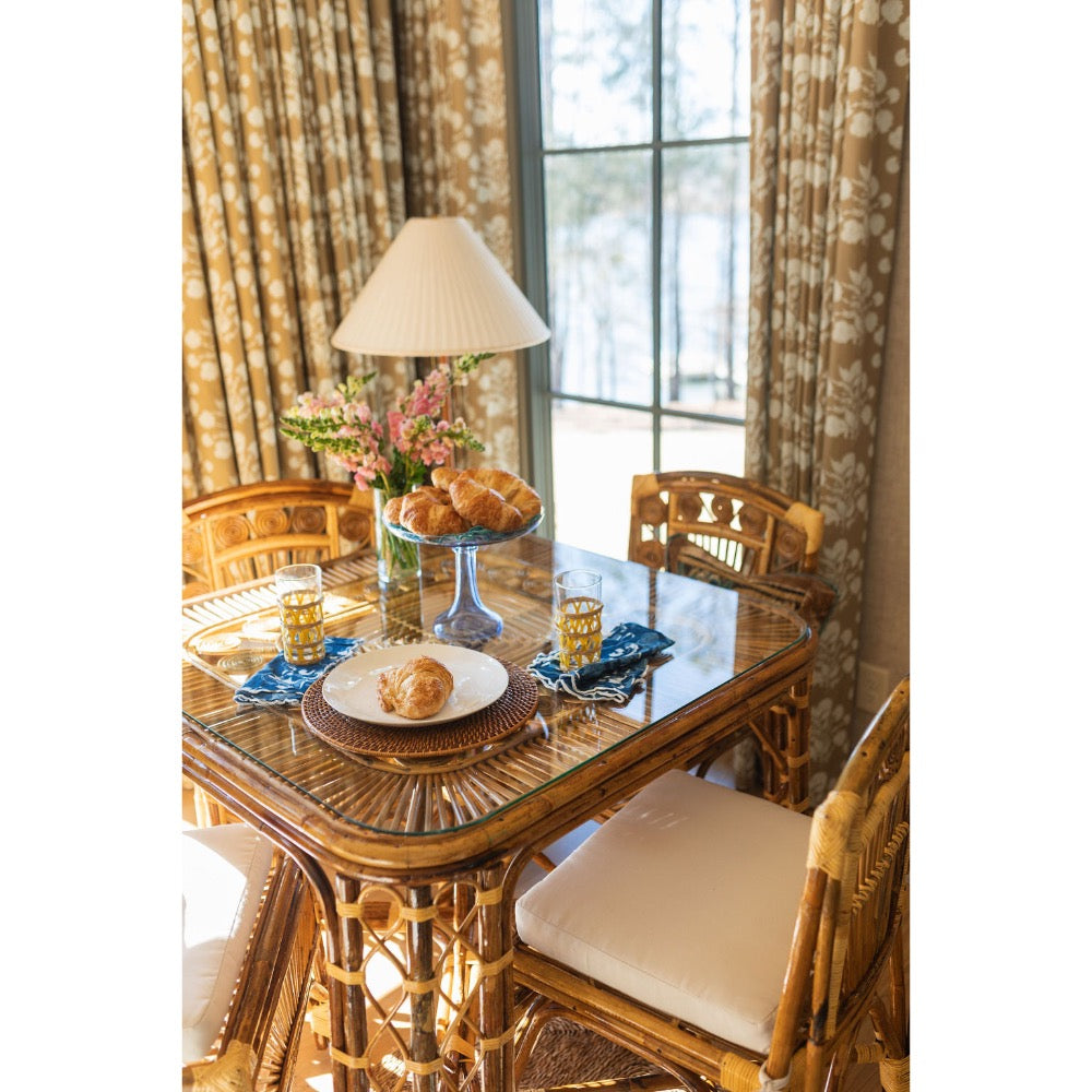 Dining room with a glass-top table and wicker chairs, featuring a floral arrangement and glasses.