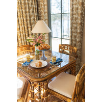 Dining room with a glass-top table and wicker chairs, featuring a floral arrangement and glasses.