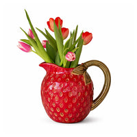 Red strawberry-shaped pitcher filled with red and pink tulips, held by a hand on a white background.