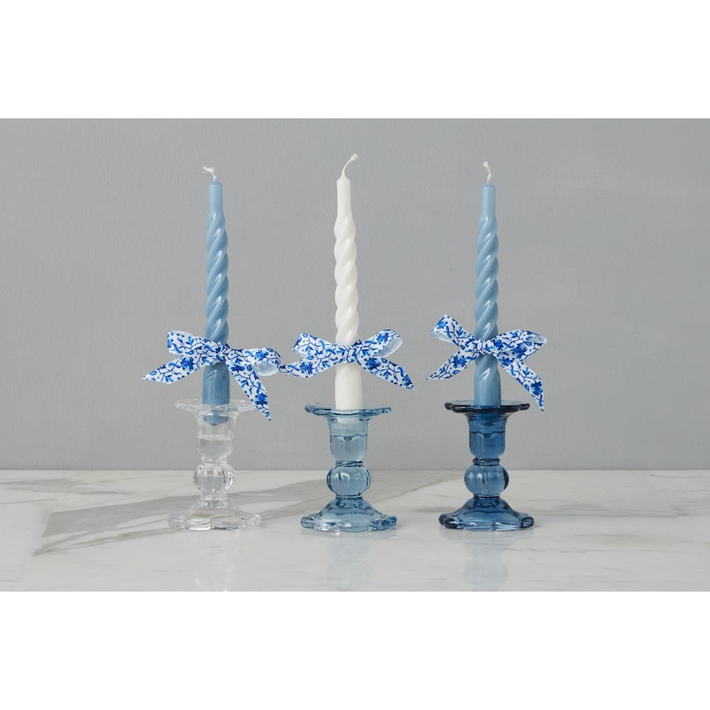 Three candlesticks with blue floral bows holding candles against a gray background