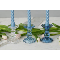 Three blue twisted candlesticks on a marble surface with green leaves and pink flowers.