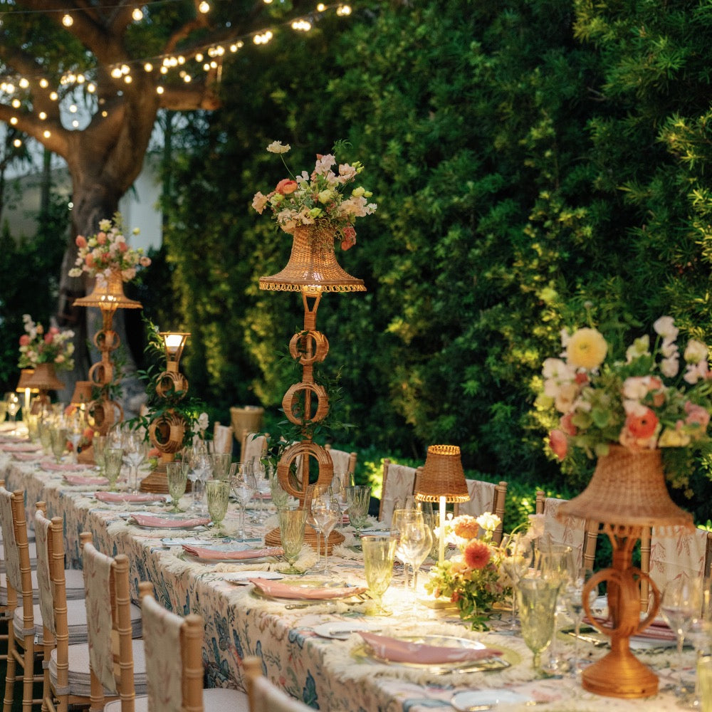 Elegant outdoor dinner table setting with floral centerpieces and string lights.