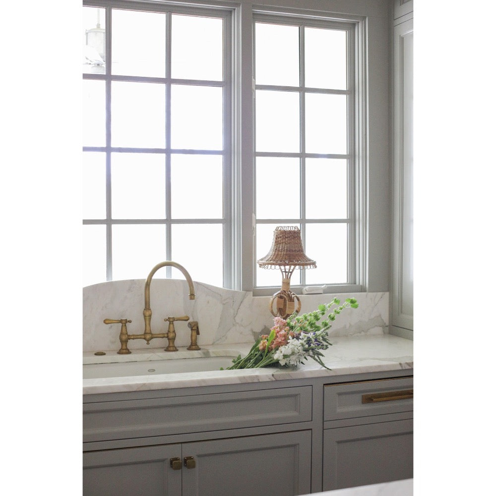 Kitchen sink area with a window above, featuring a lamp and flowers on the counter.
