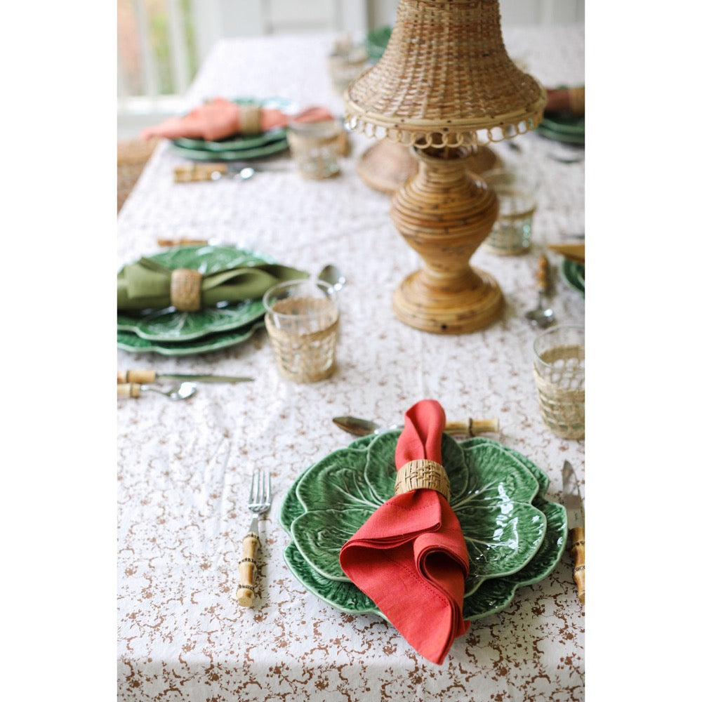 Elegant table setting with green plates, red napkins, and a wicker lamp.