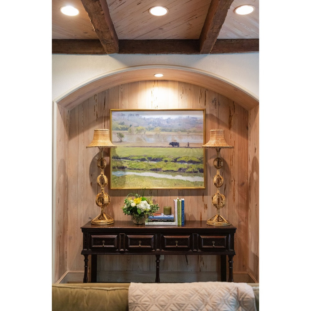 Decorative wall setup with a painting, lamps, and a console table in a room with wooden beams.