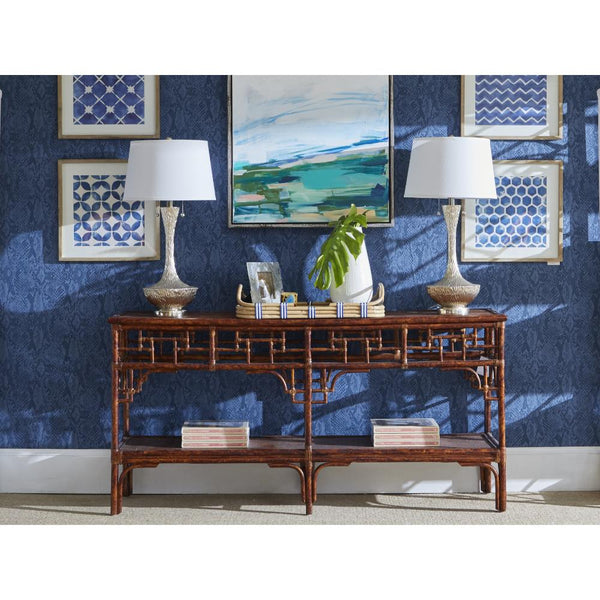 A Kenian Pagoda Rattan + Tortoise Bamboo Hall Console with lamps, books, and a plant sits by blue patterned art walls.