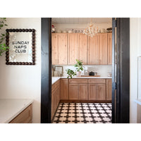 Cozy kitchen with light wood cabinets, plants, a "Sunday Naps Club" sign, and a Spicher Pattern 23 Vinyl Floorcloth.