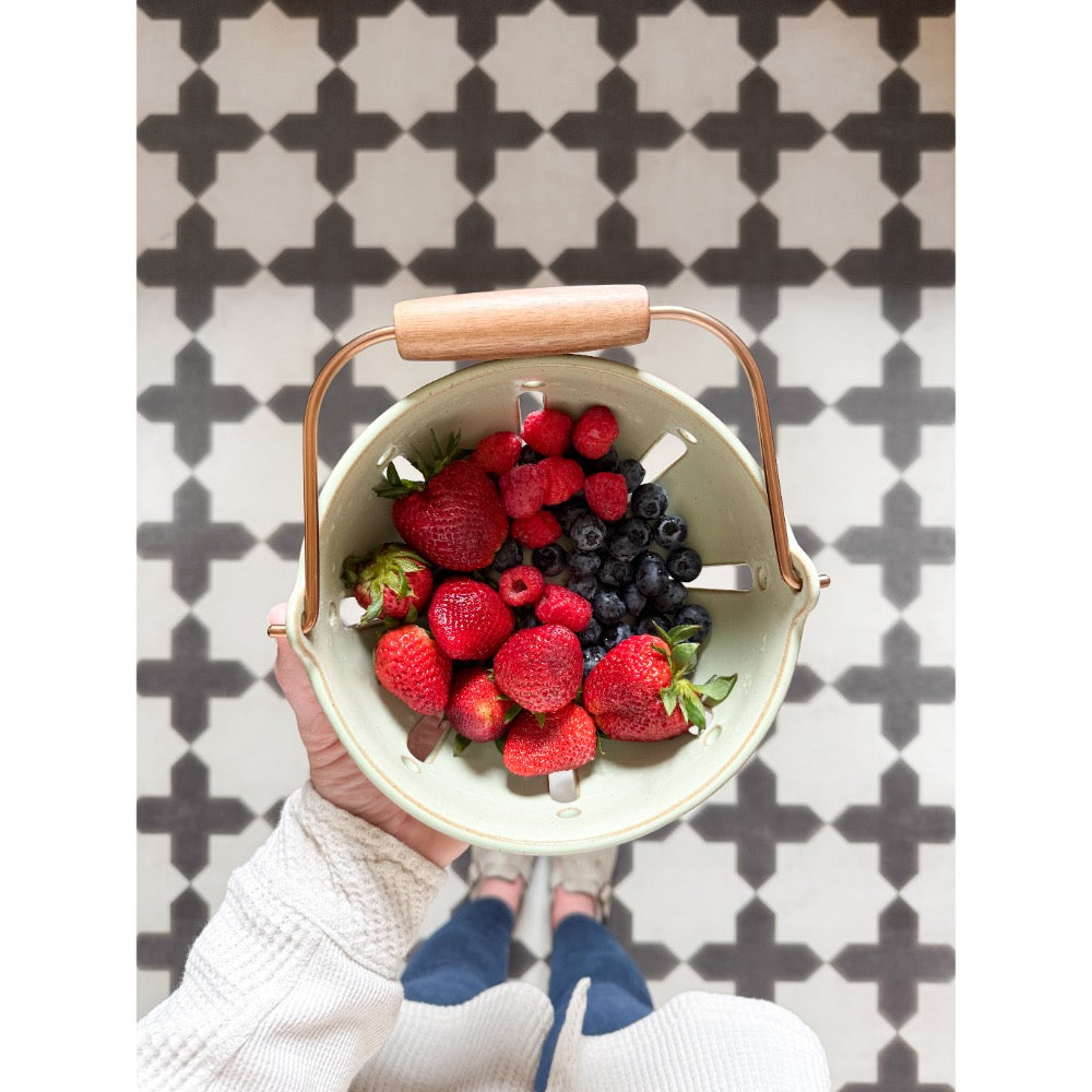 Hand holding berries over Spicher and Company's Pattern 23 Coptic Vinyl Floorcloth with a vibrant patterned design.