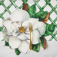 A gold fork rests on Hester & Cook's Magnolia Die Cut Paper Placemat with white magnolia and green leaves.