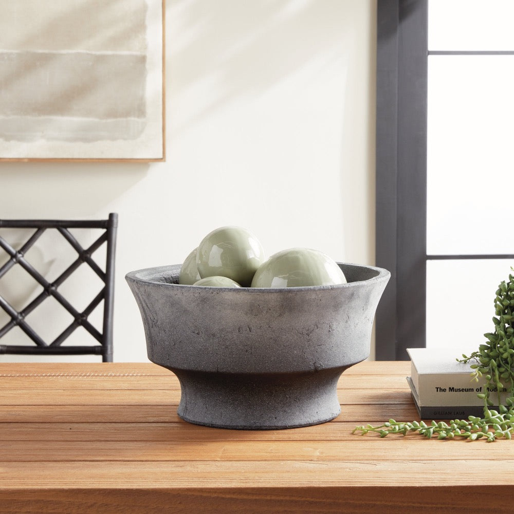 Gray stone bowl with green ceramic orbs on a wooden surface