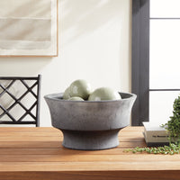 Gray stone bowl with green ceramic orbs on a wooden surface