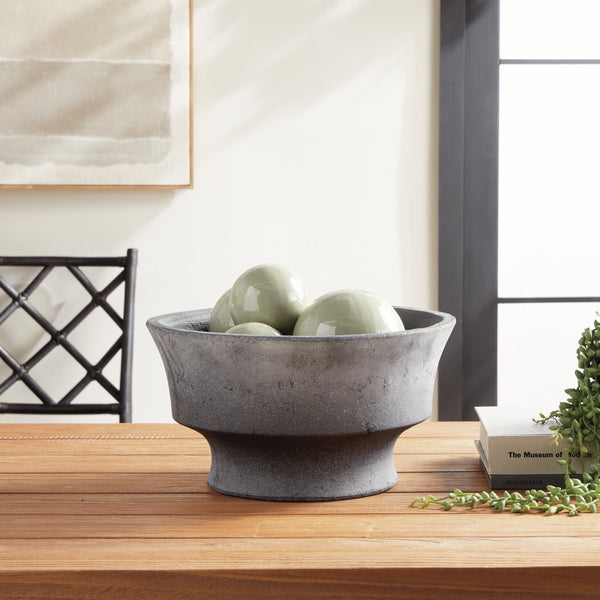 Gray stone bowl with green ceramic orbs on a wooden surface