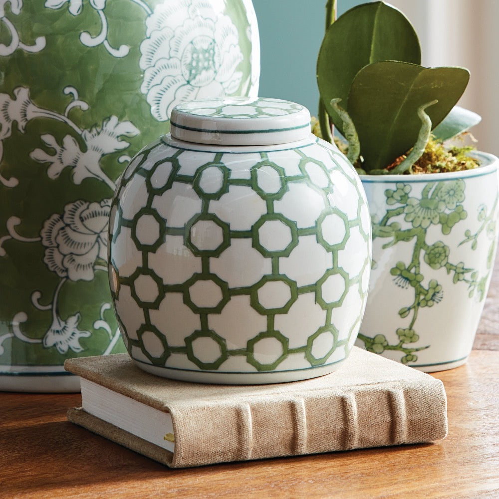 Green and white patterned ceramic jar on a book with decorative pots in the background