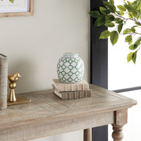 Decorative table with a green and white patterned jar, gold bird figurine, and books against a neutral wall.