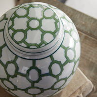 White ceramic jar with green geometric pattern on lid and body, placed indoors.